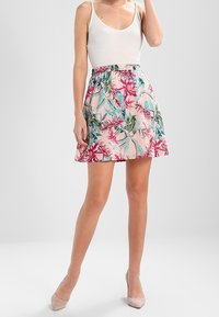 Jupe à imprimé floral avec un fond rose orné de feuilles vertes et rouges, une taille élastique et une coupe décontractée. Tissu léger.