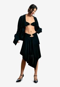 Mustast kaheosalisest komplektist koosnev rõivastus, millel on bandeautop koos kuldse pandlaga ning asümmeetriline seelik, millel on sobiv aksent. Modell kannab musti kontsakingi.