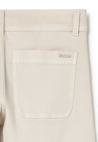 Pantalones beige con un bolsillo trasero que presenta costuras sutiles y una pequeña etiqueta de la marca. El material parece ser algodón o similar, con una textura suave.