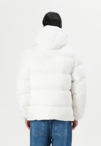 Hvid pufferjakke med hætte, der har quiltede sektioner og en glat overflade. Sammen med blå denim jeans.