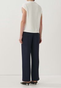 Bílý textured top s krátkými rukávy v kombinaci s vysokými navy kalhotami širokého střihu a černými botami s špičatou špičkou.