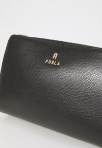 Portafoglio in pelle nera con finitura texturizzata, hardware dorato e logo impresso sul davanti. Dotato di chiusura con zip per una conservazione sicura.
