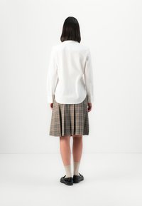 Witte langarmshirt met een gebogen zoom, gecombineerd met een grijs geruite geplooide rok. Zwarte schoenen en beige sokken maken de outfit compleet.