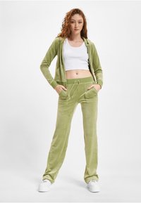 Welurowy dres w jasnym zielonym kolorze z kapturem zapinanym na zamek oraz spodniami na sznurku z przednimi kieszeniami. Biała bluzka crop top pod spodem.