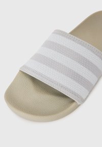 Grå slidersandal med en blød meshrem med skiftende ensfarvede og stribede mønstre samt en textured beige sål.