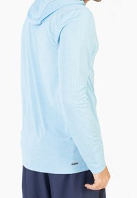 Light blue long-sleeve hoodie featuring a textured fabric with a grid pattern, adjustable hood, and a small brand logo near the hem.