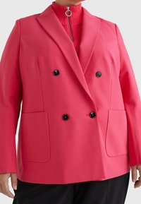 Różowa marynarka dwurzędowa z gładkiego materiału, z czarnymi guzikami i dwiema przednimi kieszeniami. Kołnierz jest wycięty, a fason jest dobrze zorganizowany.