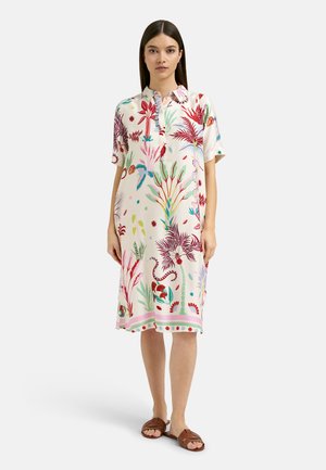 Woman wearing a knee-length, short-sleeve dress with colorful tropical plant and animal patterns, paired with brown open-toe sandals.
