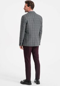 Blazer grigio a quadri con rever a nottola, spalle strutturate e vestibilità sartoriale, abbinato a pantaloni bordeaux scuro e scarpe nere.