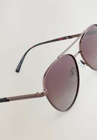 Zonnebril met een pilotenvorm, metallic roségouden montuur, gradient grijze glazen en een contrasterende rode en zwarte gepatterneerde poot.