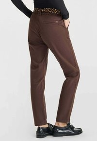 Pantaloni marroni con una cintura a stampa leopardata, design affusolato e tasche. Abbinati a scarpe nere, che mostrano una texture e una vestibilità lisce.