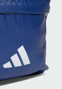 Niebieska torba z tkaniny z białym logo w postaci potrójnego pasku. Materiał wydaje się mieć fakturę i matowe wykończenie. Projekt obejmuje złożony na górze top.