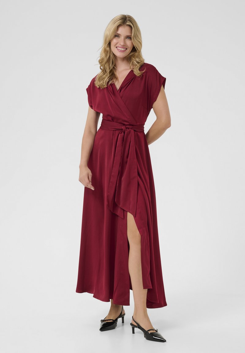 Burgundy satin omslagsklänning med korta ärmar, sidöppning och ett bälte i midjan. Bärs med svarta slingback-hälskor. Slät struktur.