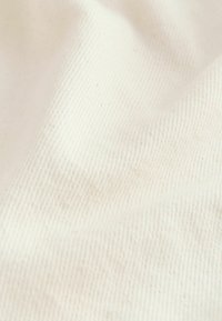 Gros plan sur un tissu texturé blanc cassé avec un motif de tissage diagonal visible et de légers plis.