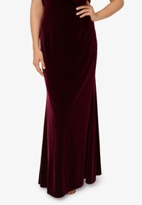 Abito maxi in velluto borgogna con una silhouette fluentemente, dotato di un corpetto aderente e leggere drappeggi, texture liscia e colore intenso.