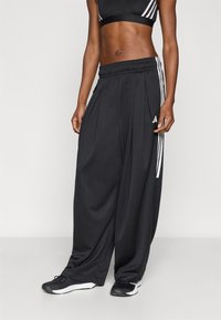 Μαύρο αθλητικό παντελόνι με φαρδιά μπατζάκια και πιέτες, με λευκές πλαϊνές ρίγες και ελαστική μέση. Συνδυάζεται με μαύρα αθλητικά παπούτσια.