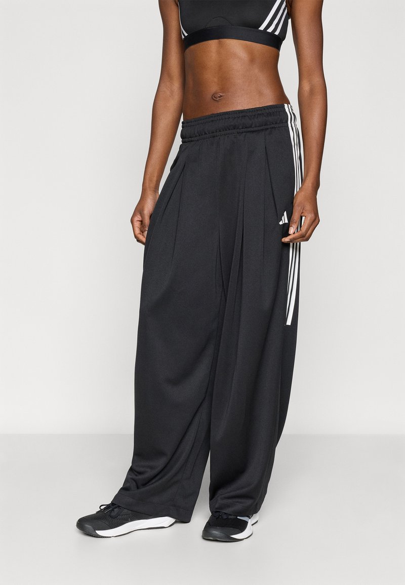 Μαύρο αθλητικό παντελόνι με φαρδιά μπατζάκια και πιέτες, με λευκές πλαϊνές ρίγες και ελαστική μέση. Συνδυάζεται με μαύρα αθλητικά παπούτσια.