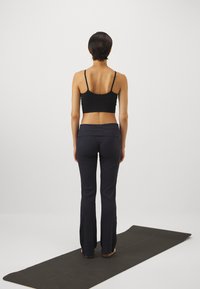Svart sports-bh og mørkeblå yoga-bukser brukt av en person på en svart yoga-matte. Antrekket har en tettsittende design og elastisk stoff.