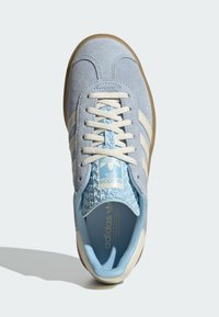 Svetlomodré semišové tenisky s bielymi pruhmi, štruktúrovaným modrým jazykom, krémovými šnúrkami a gumovou podrážkou. Na jazyku sa nachádza logo Adidas.