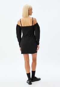 Schwarzes Off-Shoulder-Kleid mit Puff�ärmeln, tailliertem Oberteil und kurzem Saum. Verfügt über einen Reißverschluss am Rücken und hat eine glatte Textur.