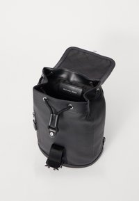 Black leather bucket bag with a drawstring closure, smooth texture, and branded tag inside. Features adjustable strap and metal hardware accents.