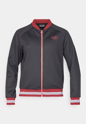 Grå zip-jakke med røde og hvite stripede mansjetter og falde. Har en rød logo på brystet og en ribbet krage. Glatt stofftekstur.