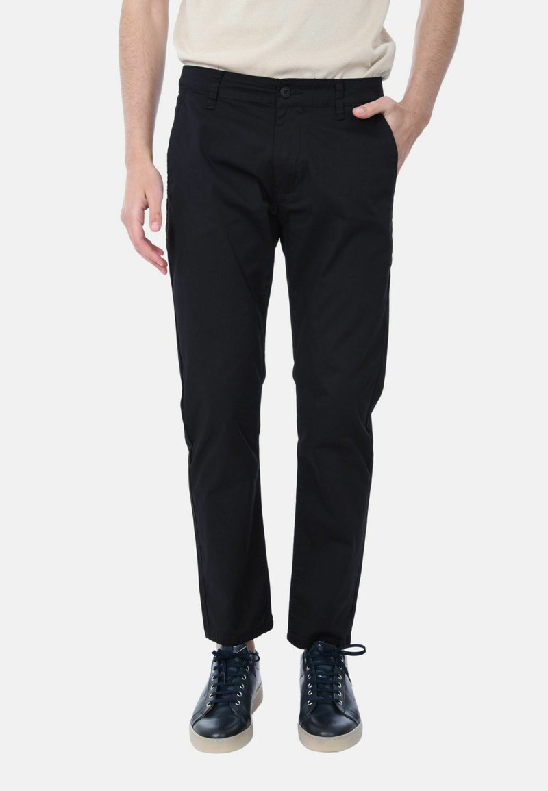 Pantaloni in cotone neri con vestibilità dritta, dotati di chiusura a bottone, tasche laterali e indossati con sneaker blu navy.