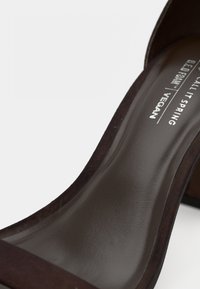 Σκούρο καφέ vegan πέδιλο με ψηλό τακούνι, με λείο φινίρισμα, ανοιχτή μύτη και φαρδιά λουρίδα στο μπροστινό μέρος. Το κείμενο στην εσωτερική σόλα γράφει "B.E.D.G.R.A.M. | VEGAN."