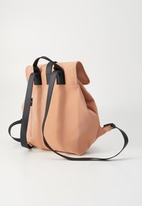 Parkerosa ryggsekk laget av glatt materiale, med svarte stropper, lokk på toppen og en sidelomme med glidelås.