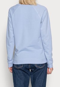 Sudadera azul claro hecha de material suave, con un escote redondeado, puños y dobladillo acanalados. La parte trasera tiene una textura suave y un detalle minimalista.