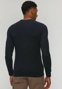 Maglione lavorato a maglia blu navy con maniche lunghe, caratterizzato da un motivo testurizzato e un collo rotondo a coste. Indossato al rovescio, mostrando il dettaglio sul retro.