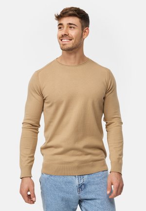 Beige gebreide trui met een ronde halslijn, geribde manchetten en tailleband. De textuur is glad met een aansluitend ontwerp. Gecombineerd met lichtblauwe jeans.