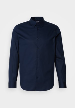 Sötétkék, hosszú ujjú ing sima anyagból, gombos elülső résszel, hegyes gallérral és mandzsettákkal, a mellkason diszkrét logóval.