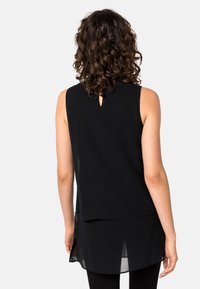 Débardeur noir sans manches avec un détail dos en œillet, design superposé et texture lisse. L'ourlet est plus long à l'arrière avec des fentes sur les côtés.