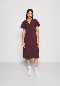 Burgundy wrap dress with short flutter sleeves, mid-calf length, lightweight texture. Worn with white sneakers and ankle-length socks.
