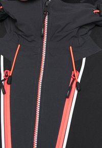 Zwart-grijze jas met een contrasterende rode ritssluiting, witte accenstrepen en een verstelbare capuchon met trekkoord. Gladde, technische stoftextuur.