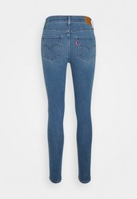 Jeans ajustados de color azul, confeccionados en denim con una textura suave, que presentan un parche en la cintura, dos bolsillos traseros y costuras intactas a lo largo de las uniones.