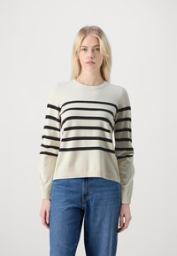 Cremefarbener Pullover mit schwarzen horizontalen Streifen, Rundhalsausschnitt, langen Ärmeln und Rippenbündchen. Kombiniert mit blauen Jeans.