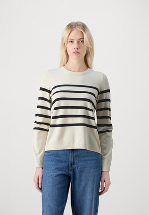 Kremfarget genser med svarte horisontale striper, rund hals, lange ermer og ribbestrikket kant. Kombinert med blå denimjeans.