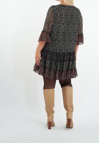 Vestido negro con flores, con volantes en capas y mangas de campana, que presenta una superposición transparente. Combinado con botas de serpiente de color marrón hasta la rodilla.