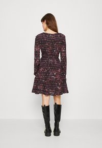 Vestido preto com flores, mangas longas, cintura franzida e bainha em camadas com babados. Combinado com botas pretas até ao joelho, apresenta um padrão roxo e amarelo.