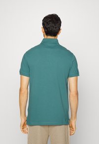 Polo shirt teal à coupe décontractée, à manches courtes et col côtelé. Détails minimalistes, coutures visibles et texture en coton doux.