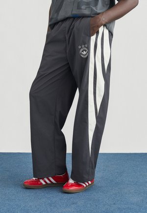 Sivé športové nohavice s bielymi pruhmi po stranách a logom s hviezdami. Kombinované s červenými topánkami s bielymi pruhmi a gumovou podrážkou.