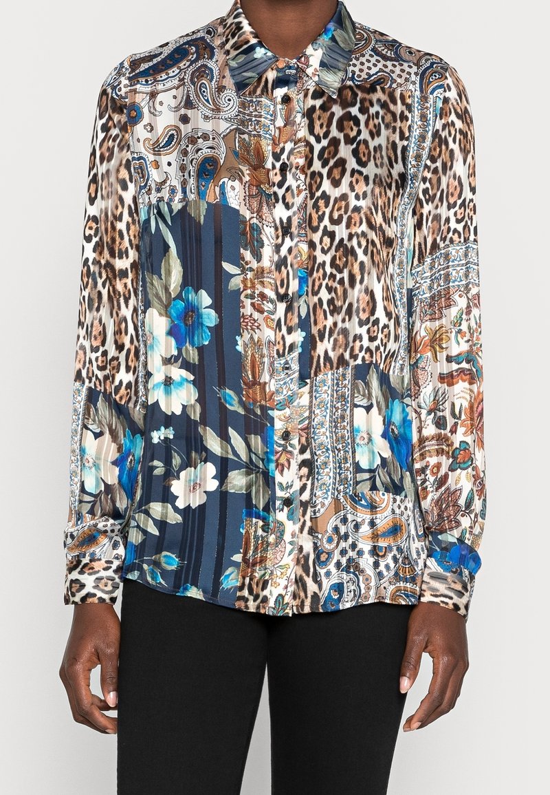 Blouse à manches longues avec boutons, présentant des motifs mixtes incluant des taches de léopard, des fleurs bleues et des motifs paisley dans des tons marron, bleu et blanc.