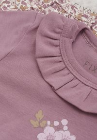 Chemise lavande avec un col en volants, ornée d'un imprimé floral en rose clair et vert, fabriquée en coton doux.