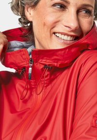 Rote wasserdichte Jacke mit hohem Kragen, Reißverschluss und verstellbaren Kordelzügen. Verfügt über eine glatte Textur und graue Innenausstattung.