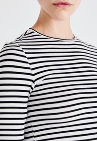Black and white striped long-sleeve shirt with a crew neck. Soft textile, fitted design, featuring evenly spaced horizontal stripes.