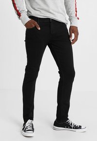 Svarta denimjeans med smal passform, som har fem fickor och en slät yta. Dessa är kombinerade med svarta kanvas skor och en grå långärmad tröja.