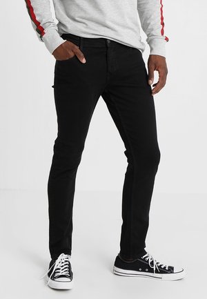 Jeans de mezclilla negra con un corte ajustado, que disponen de cinco bolsillos y una textura suave. Combinados con zapatos de lona negros y una camisa de manga larga gris.