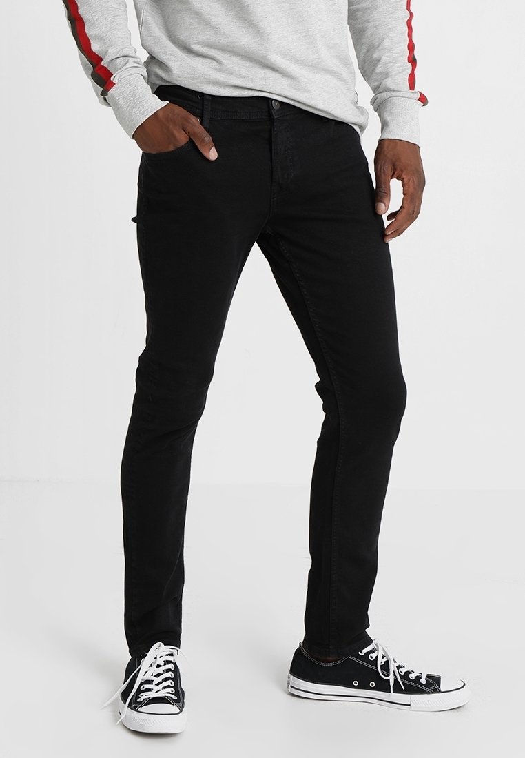 Svarta denimjeans med smal passform, som har fem fickor och en slät yta. Dessa är kombinerade med svarta kanvas skor och en grå långärmad tröja.